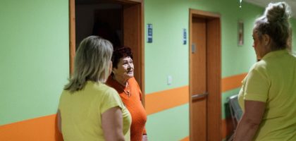 Senior woman engages in conversation with caregivers in a facility corridor.