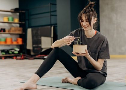 Young woman enjoying a healthy salad after exercising indoors. Promotes a balanced diet and fitness lifestyle.