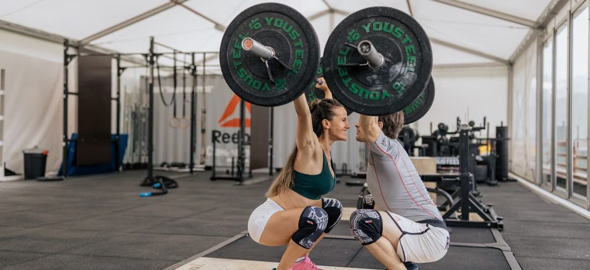 A couple lifting weights together in a gym, promoting fitness and teamwork.